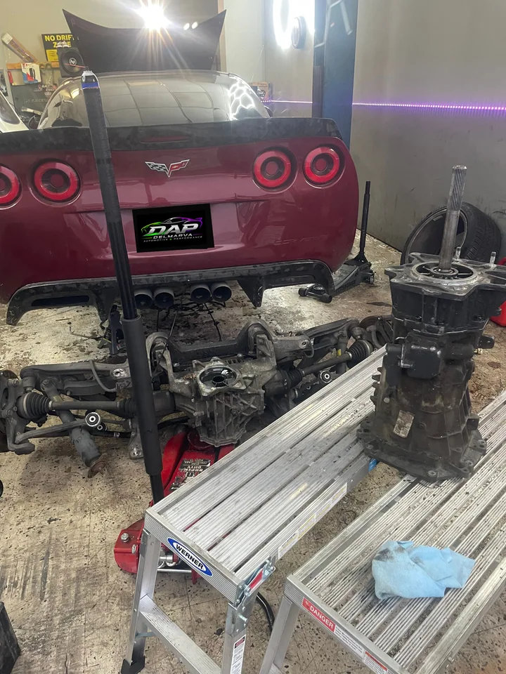 Corvette with drivetrain components laid out nearby; plate covered with the DAP logo
